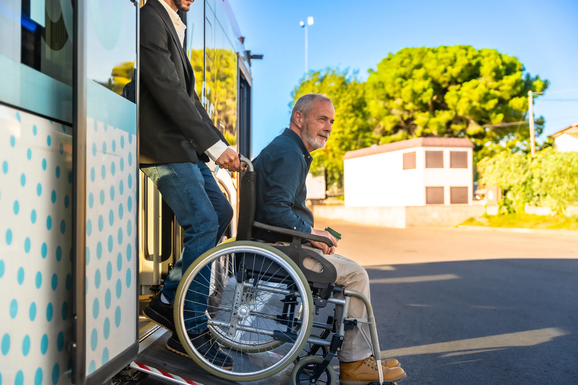Assistant helping a man in a wheelchair board an accessible vehicle