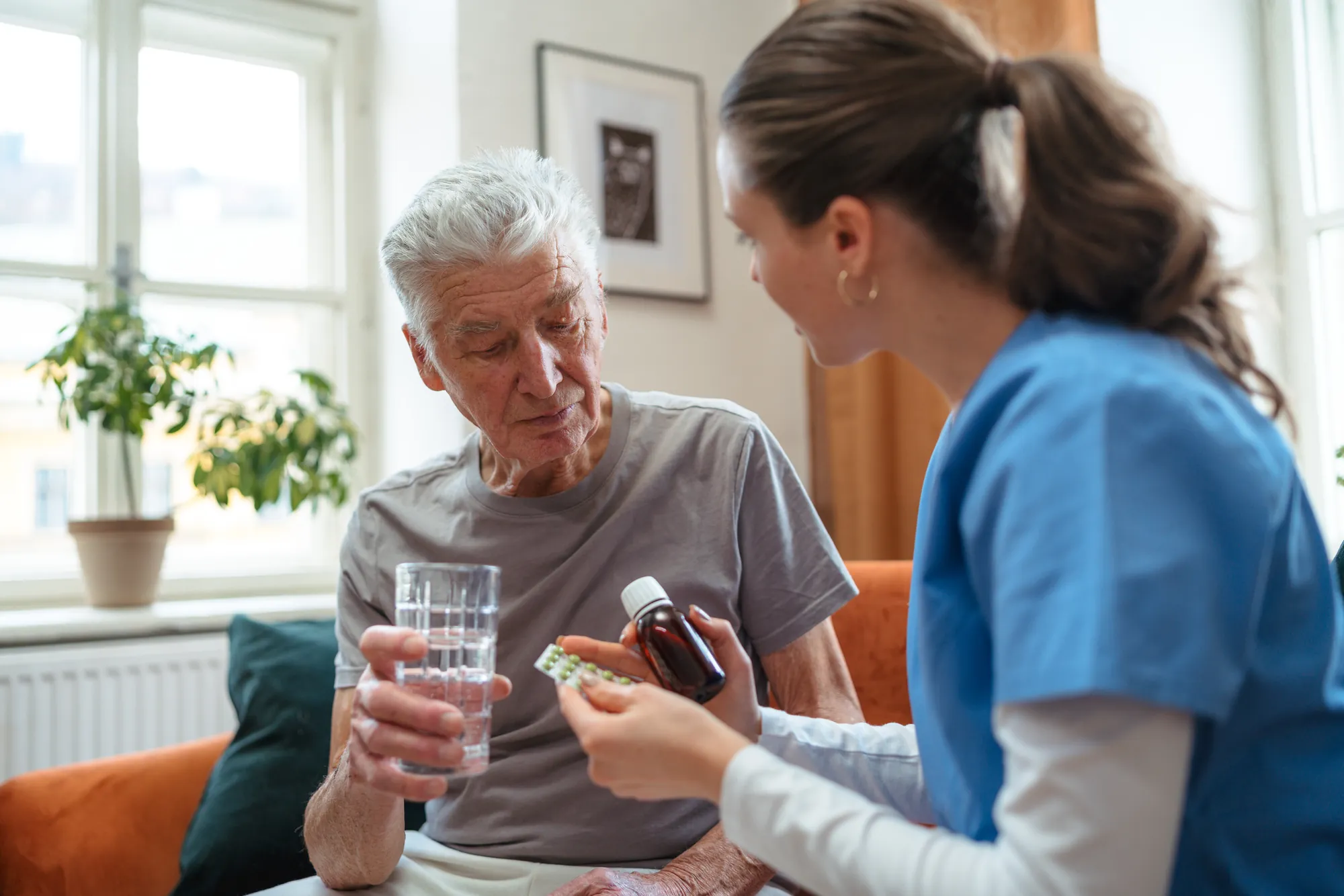 Caregiver handing a senior man his medication and a glass of water