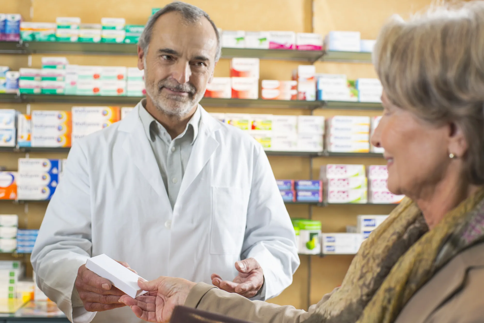 Pharmacist handing a prescription to a senior woman at the counter