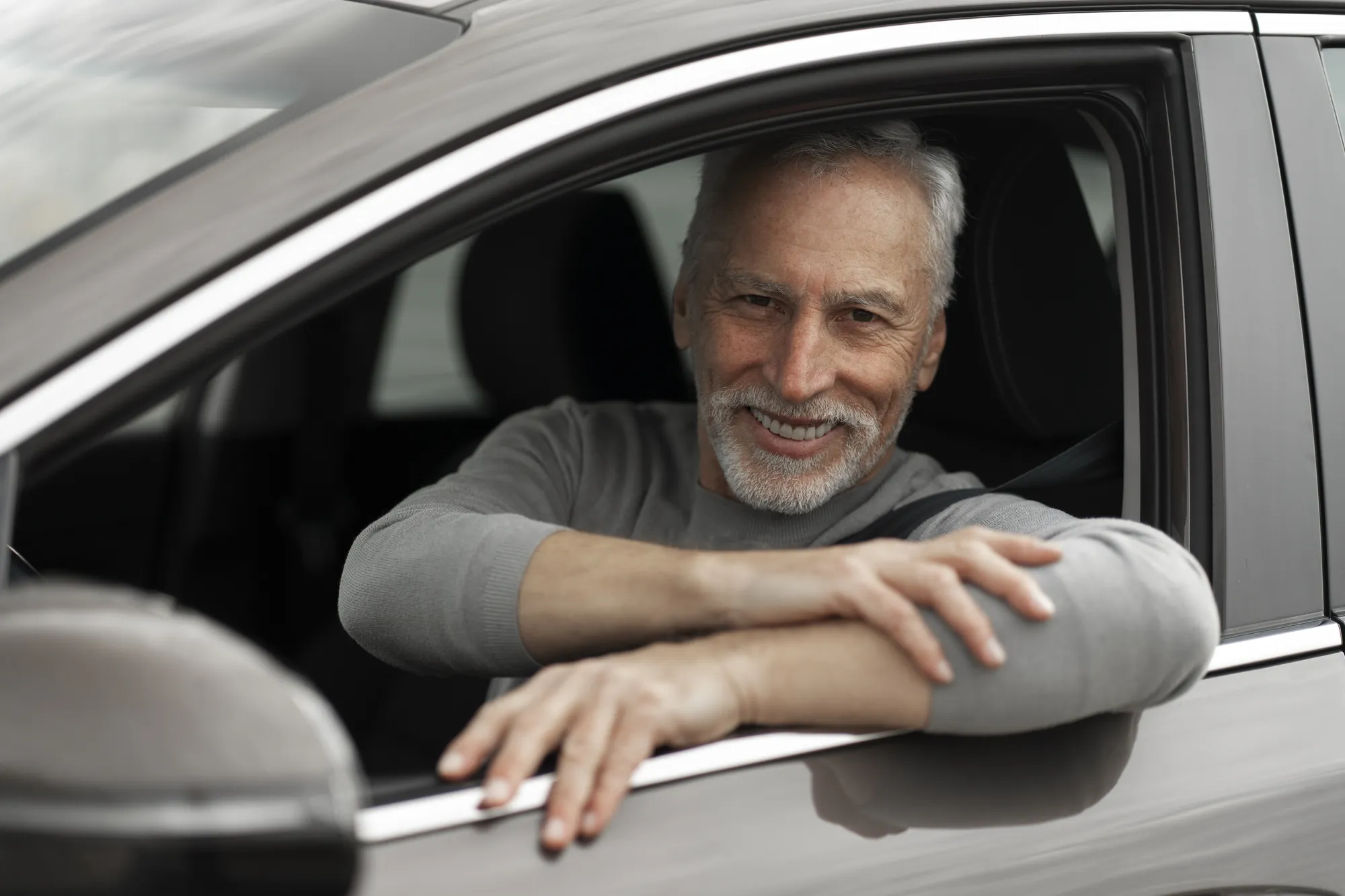 Senior man smiling as he leans on the open window of a car
