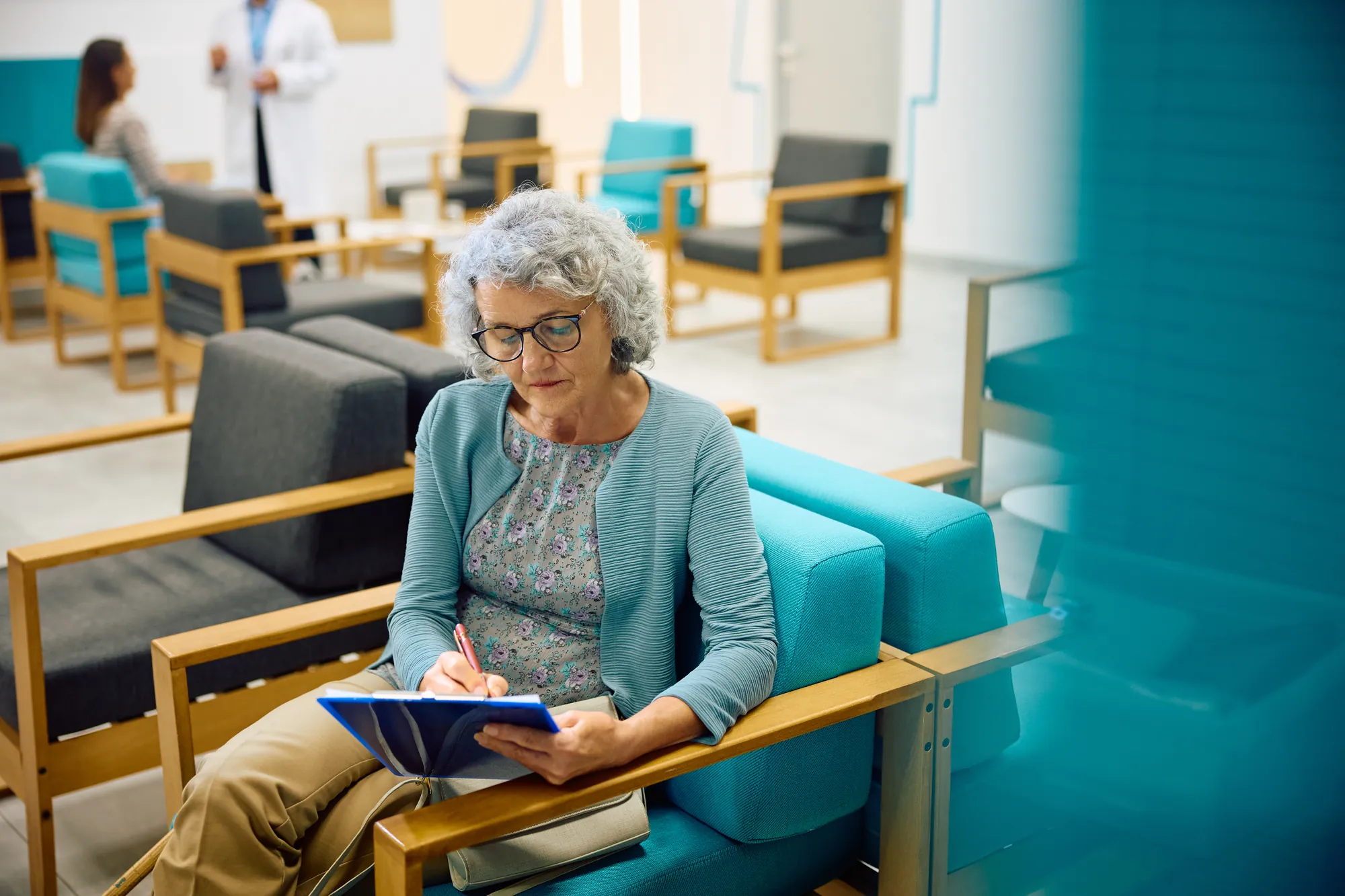 Senior woman filling out a form on teal chairs in a waiting room