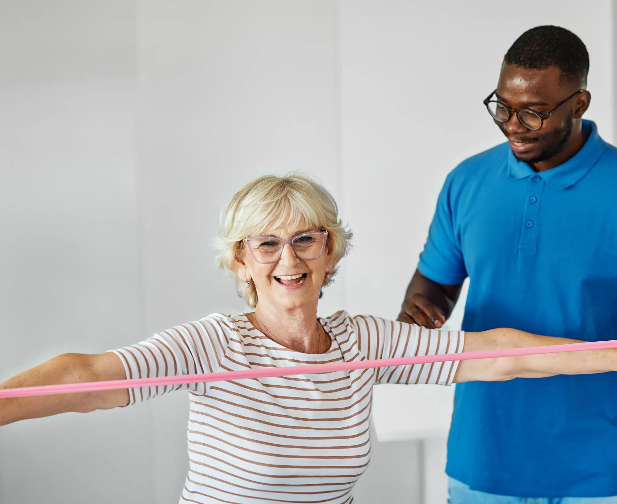 Smiling senior woman exercising with a resistance band beside her therapist
