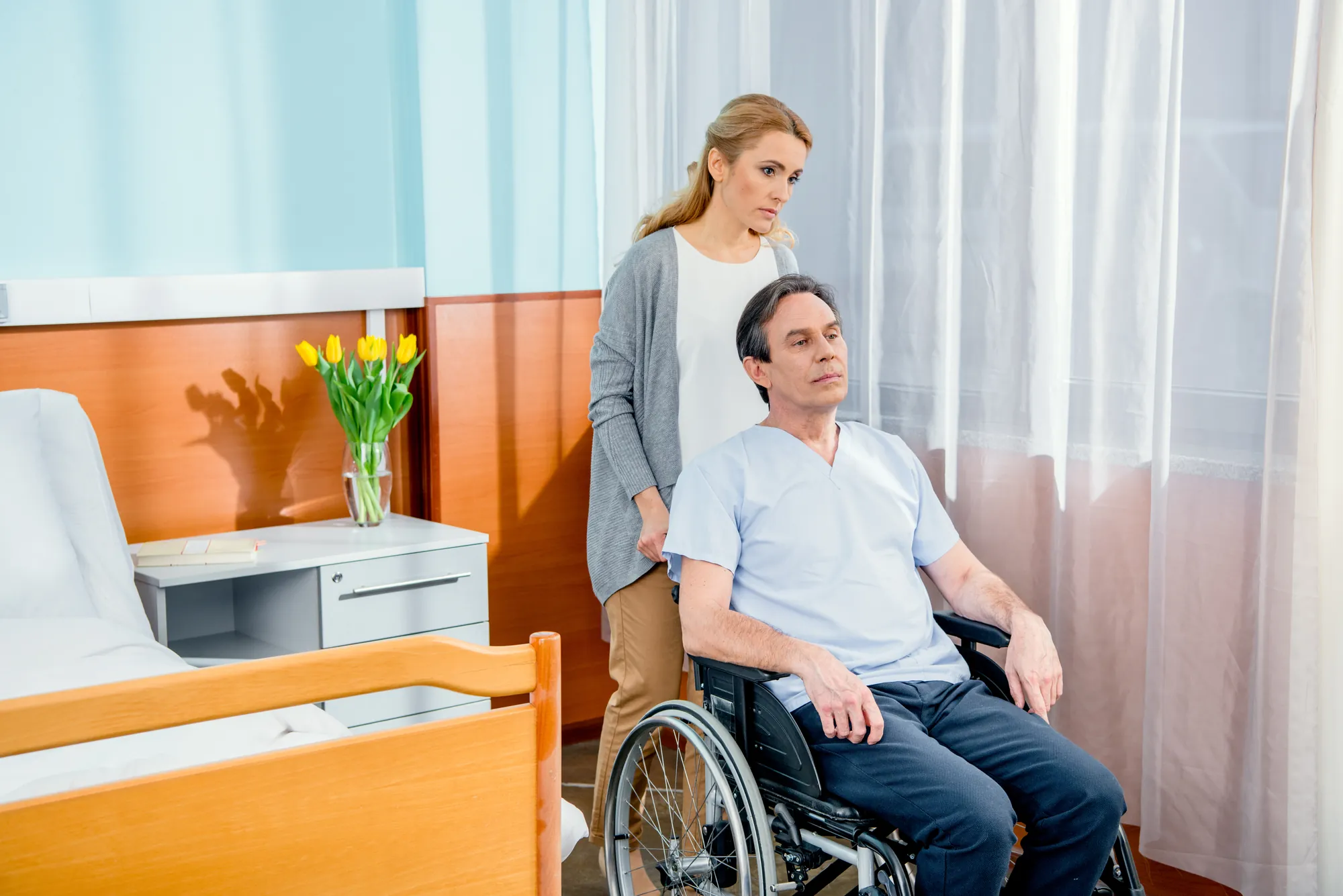 Woman standing beside a man in a wheelchair in a bright hospital room